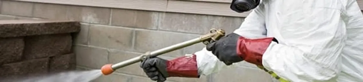 Pest control technician applying exterior insect treatment along a home foundation in Eugene, OR