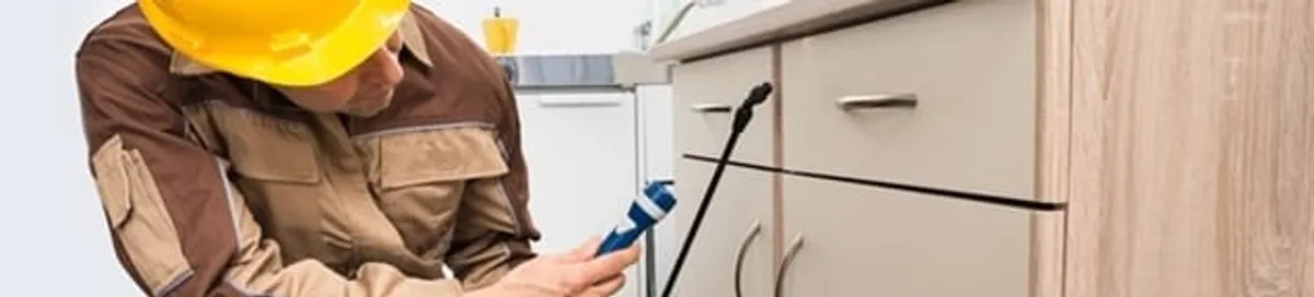 Roach exterminator applying treatment under kitchen cabinets in Eugene, OR