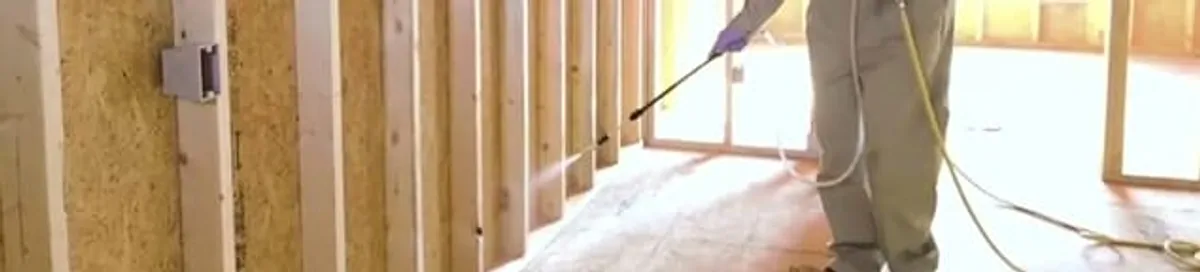 Termite treatment technician applying spray along framing and unfinished walls in Eugene, OR